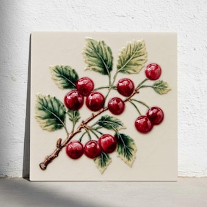 以下が含まれることがあります： 桜の枝のレリーフが施された正方形のセラミックタイル。サクランボは光沢のある赤色、葉は緑と黄色、枝は茶色です。タイルはクリーム色の背景です。