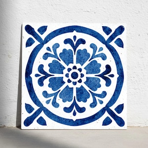 Puede incluir: Azulejo cuadrado blanco con diseño floral azul. El azulejo presenta un motivo floral central rodeado por un círculo y detalles en las esquinas. El diseño azul oscuro contrasta con el fondo blanco.