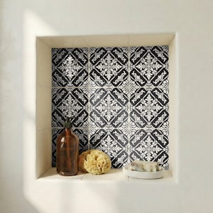Puede incluir: Un estante empotrado en el baño con azulejos estampados en blanco y negro. El estante contiene una botella de vidrio marrón, una esponja natural y un plato blanco pequeño con jabón. Los azulejos tienen un diseño floral repetido.