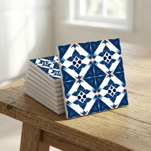 Può includere: Una pila di piastrelle quadrate in ceramica con un motivo floreale blu e bianco. Le piastrelle presentano un design ripetuto di fiori stilizzati e forme geometriche. Le piastrelle sono esposte su una superficie di legno.