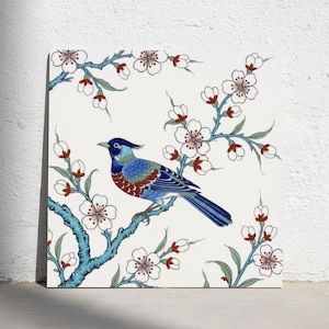 May include: A square wall art print featuring a blue bird with a crest perched on a branch of white cherry blossoms. The branches are blue with green leaves and red accents, set against a plain white background in a detailed illustration.