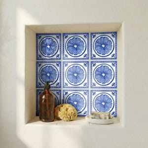 Può includere: Una nicchia del bagno presenta piastrelle decorative blu e bianche con un design di agrumi. Sono visibili anche un dosatore di sapone marrone, una spugna naturale e una saponetta su un piatto bianco.
