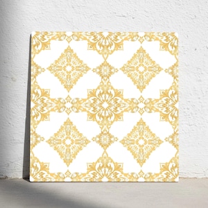 以下が含まれることがあります： 白い背景に金色の花柄模様が繰り返される正方形のキャンバス。このパターンは、対称的で装飾的なモチーフを特徴とし、装飾的でエレガントな美学を作り出しています。このアートワークは白い壁に展示されています。