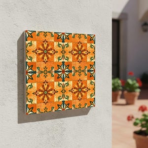 May include: Square wall art featuring a repeating pattern of orange, green, and cream-colored floral and geometric designs. The artwork is mounted on a white wall, showcasing a vibrant, decorative tile motif.