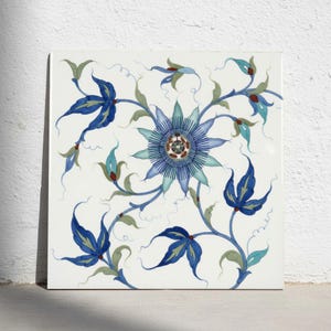 Könnte beinhalten: Eine quadratische Keramikfliese mit einer zentralen blauen Passionsblume, umgeben von fließenden Ranken und Blättern in Blau-, Türkis- und Salbeigrüntönen. Das Design ist auf einem weißen Hintergrund mit zarten, dünnen Ranken angeordnet.