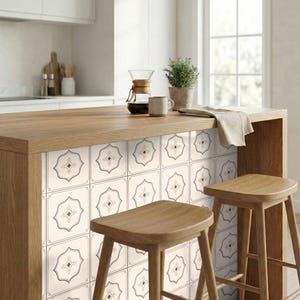 Puede incluir: Isla de cocina con encimera de madera clara y azulejos decorativos. El azulejo presenta un fondo crema con un diseño geométrico negro y dorado. Dos taburetes de madera están frente a la isla. Una cafetera, una taza y una planta están en la encimera.