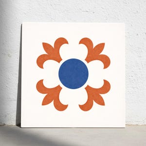 Puede incluir: Azulejo cuadrado blanco con un diseño floral simétrico. El diseño presenta un círculo azul central rodeado de cuatro formas anaranjadas en forma de pétalo. El azulejo está colocado contra una pared blanca.