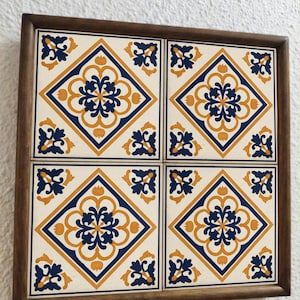 Könnte beinhalten: Ein quadratischer Holzrahmen mit vier dekorativen Fliesen. Jede Fliese zeigt ein sich wiederholendes Muster aus blauen und goldenen floralen Designs auf cremefarbenem Hintergrund. Die Fliesen sind in einem 2x2-Raster angeordnet.