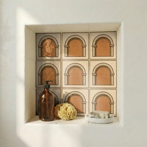 May include: A bathroom alcove with square tiles featuring an arch design in brown and beige. A brown soap dispenser, a natural sponge, and a white soap dish with soap are on the shelf.