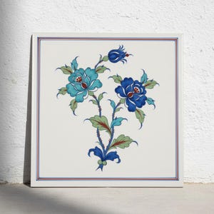Op de afbeelding: Een vierkante keramische tegel met een centraal bloemmotief met twee grote bloemen in tinten turkoois en diepblauw, geaccentueerd door groene bladeren en stengels. Het ontwerp is ingesloten in een dunne rode en blauwe dubbele lijnrand.