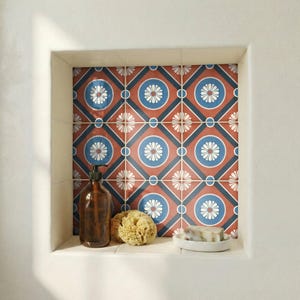 May include: A bathroom niche with decorative tiles featuring a red, blue, and white floral pattern. The niche contains a brown soap dispenser, a natural sponge, and a small white soap dish with a bar of soap.