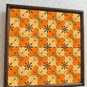 May include: A framed decorative tile with a repeating pattern. The design features orange, yellow, and brown floral motifs. The frame is a dark brown color, and the tile is mounted on a white wall.