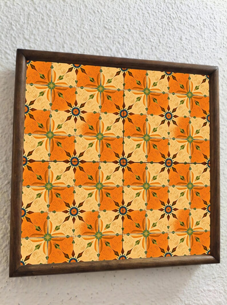 May include: A framed decorative tile with a repeating pattern. The design features orange, yellow, and brown floral motifs. The frame is a dark brown color, and the tile is mounted on a white wall.