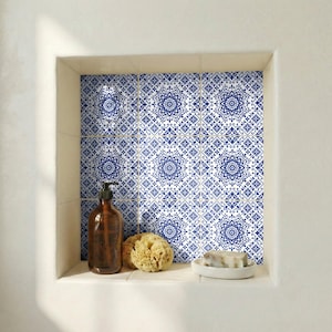 Puede incluir: Un estante empotrado en el baño con azulejos estampados en azul y blanco. El estante contiene un dispensador de jabón marrón, una esponja natural y un plato blanco pequeño con jabón. Los azulejos presentan un diseño floral.