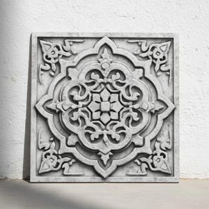 Può includere: Piastrella da parete decorativa quadrata grigia con un ornato e simmetrico motivo floreale. La piastrella presenta un motivo intagliato in rilievo con un fiore centrale e volute circostanti. La piastrella è realizzata in un materiale simile alla pietra.