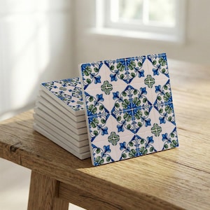 以下が含まれることがあります： 白を基調に青と緑の花柄が繰り返される正方形のセラミックタイルのスタック。 タイルは木製の表面に表示されています。