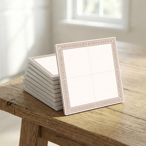 Puede incluir: Una pila de posavasos cuadrados con un centro blanco y un borde decorativo marrón. Los posavasos están apilados sobre una superficie de madera, con un posavasos enfocado, mostrando el diseño.