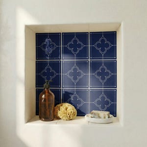 Puede incluir: Un nicho de baño empotrado con azulejos azul marino con un diseño de cuatrifolio blanco. El nicho contiene una botella de vidrio marrón con una bomba, una esponja natural y un jabonera blanca con una pastilla de jabón.