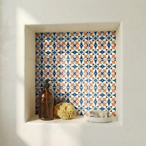 May include: A built-in bathroom shelf with patterned tiles in blue, orange, and white. The shelf holds a brown soap dispenser, a natural sponge, and a small white soap dish with a bar of soap.