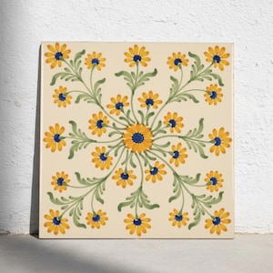 Könnte beinhalten: Eine quadratische Keramikfliese mit cremefarbenem Hintergrund und einem symmetrischen Blumenmuster. Das Design besteht aus gelben, gänseblümchenartigen Blüten mit dunkelblauen Zentren und grünen Stielen in einem kreisförmigen Motiv.