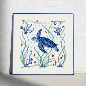 May include: A square ceramic tile featuring a central blue sea turtle swimming amidst stylised light green seaweed, small blue bubbles, and scattered red coral branches, all framed by a thin blue border on a white background.