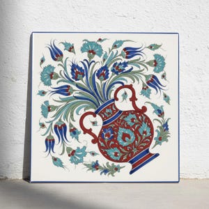 May include: A square ceramic tile featuring a central red vase with blue and white floral patterns. The vase is surrounded by a vibrant arrangement of blue and red tulips and carnations with green stems, all set against a white background.
