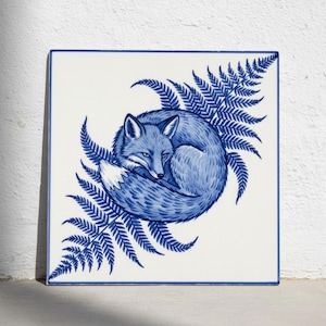 May include: A square ceramic tile featuring a blue and white illustration of a curled-up fox nestled among fern fronds. The design uses a classic blue ink style on a white background, with a thin blue border framing the entire square tile.