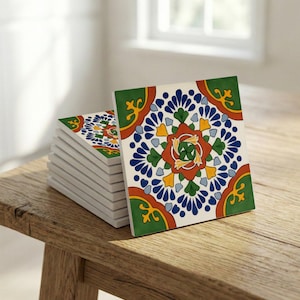 May include: A stack of square ceramic tiles with a colorful floral design. The tiles feature a white background with a central pattern of blue, orange, green, and yellow. The tiles are stacked on a wooden surface.