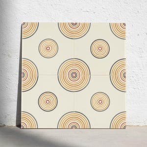 May include: A square tile featuring a repeating pattern of concentric circles in shades of orange, yellow, and dark grey against a cream-coloured background. The design consists of larger circles centred in the middle and smaller circles in the corners.