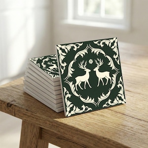 May include: A stack of square ceramic tiles with a dark green background and a white deer design. The tiles feature a decorative border with floral elements. The tiles are stacked on a wooden surface.