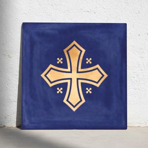 May include: A square, navy blue tile with a gold-coloured cross design. The cross has a detailed outline and is centred on the tile. Small, gold-coloured cross-like shapes are in each corner of the cross.