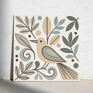 Op de afbeelding: Vierkante keramische tegel met een beige vogel, accenten in grijs en beige, omringd door gestileerde bladeren en stippen in grijstinten, blauw en beige. Het ontwerp is geplaatst tegen een witte achtergrond en creëert een decoratief en artistiek stuk.
