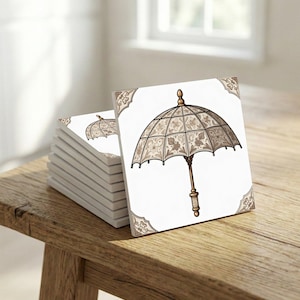 May include: A stack of white square tiles with a sepia-toned umbrella design. The umbrella features a detailed floral pattern and a wooden handle. Decorative corner accents complement the design. The tiles are stacked on a wooden surface.