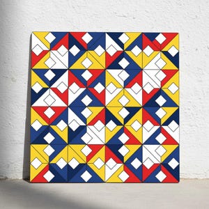 May include: A square artwork featuring a geometric pattern of red, yellow, blue, and white shapes. The design includes diamonds and triangles arranged in a repeating, symmetrical layout. The artwork is displayed against a white wall.