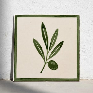 Puede incluir: Azulejo cerámico cuadrado con fondo crema y diseño de rama de olivo verde. La rama de olivo presenta hojas verdes y una sola aceituna. El azulejo tiene un borde verde.