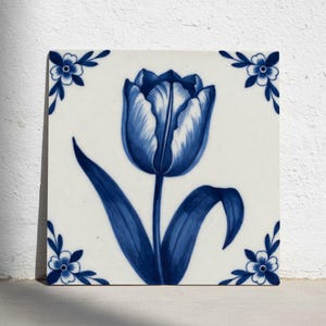 Könnte beinhalten: Quadratische Keramikfliese mit handgemaltem blauen Tulpenmotiv. Die Tulpe ist auf weißem Hintergrund zentriert, mit blauen floralen Eckakzenten. Die Fliese ist wahrscheinlich für dekorative Zwecke.