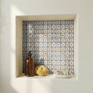 May include: A built-in bathroom shelf with nautical-themed tiles. The tiles feature anchors, fish, and seashells in blue, white, and tan. A brown soap dispenser, a natural sponge, and a bar of soap on a white dish are on the shelf.