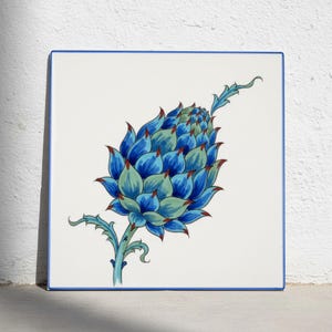 Könnte beinhalten: Eine quadratische Keramikfliese mit weißem Hintergrund und blauem Rand. In der Mitte befindet sich eine handgemalte Illustration einer stilisierten Artischocke oder Distelblüte in Blau- und Hellgrüntönen mit spitzen, rot gefärbten Blättern.