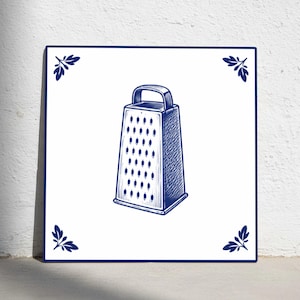 May include: A square, white tile with a blue and white illustration of a box grater. The grater is centered on the tile, with a handle at the top. Blue leaf designs are in each corner.