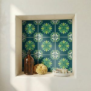 Puede incluir: Un nicho de baño con azulejos florales turquesa, un dispensador de jabón marrón, una esponja natural y una pastilla de jabón en un plato blanco. Los azulejos presentan un patrón repetido de flores estilizadas verdes y blancas.
