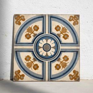 May include: Four square ceramic tiles with a floral design. The tiles have a cream background with blue and brown floral patterns. The design includes a central flower and corner floral accents.