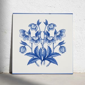 May include: A square ceramic tile featuring a symmetrical blue and white illustration of hellebore flowers and leaves. The design displays multiple blossoms and buds arranged in a central cluster against a plain white background.