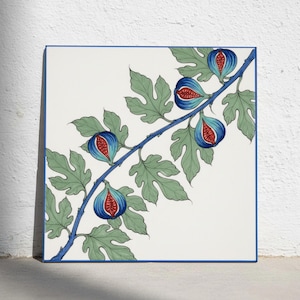 Op de afbeelding: Een vierkante keramische tegel met een witte achtergrond en een blauwe rand. Het ontwerp toont een diagonale tak met lichtgroene gelobde bladeren en vijf gehalveerde vijgen met donkerblauwe schillen en felrood vruchtvlees.