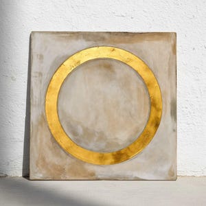 Könnte beinhalten: Quadratische Kunst mit einem goldenen Kreis auf neutralem Hintergrund. Der goldene Kreis ist auf dem Quadrat zentriert und schafft ein minimalistisches und modernes Design. Das Kunstwerk hat ein strukturiertes Aussehen.