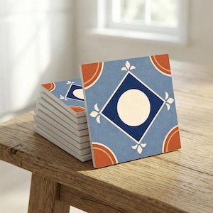 May include: A stack of square ceramic tiles with a blue background, a white circle, and a dark blue diamond in the center. The tiles have orange and white decorative accents. The tiles are stacked on a wooden surface.