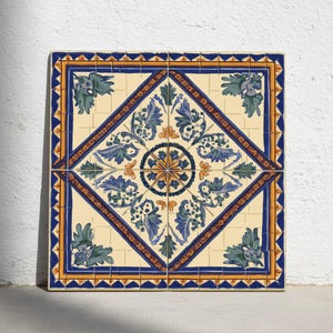 Op de afbeelding: Vier vierkante keramische tegels die samen een groter vierkant vormen. Elke tegel heeft een crèmekleurige achtergrond met een centraal ruitpatroon van blauwe bladeren en bloemmotieven. De tegels zijn omlijst met blauwe en gouden accenten.