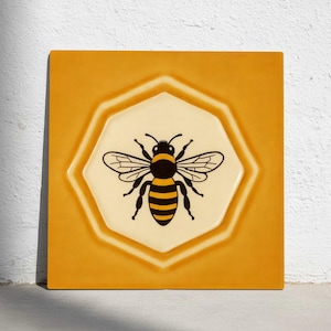 Può includere: Piastrella quadrata in ceramica con un disegno di ape. La piastrella presenta un bordo giallo e un centro ottagonale color crema. L'ape è nera e gialla con ali dettagliate.