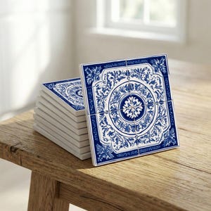 May include: A stack of square ceramic tiles with a blue and white floral design. The tiles are arranged on a wooden surface, with a few tiles standing upright, showcasing the intricate pattern. The design features a central medallion surrounded by detailed botanical elements.