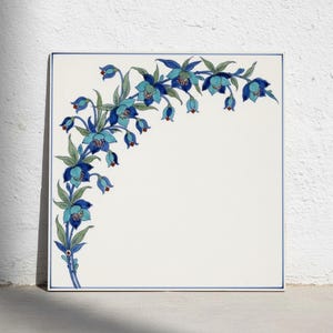 May include: A square ceramic tile with a white background and a thin blue border. A decorative floral pattern of blue and turquoise columbine flowers with green leaves curves along the left and top edges, leaving the center area blank.