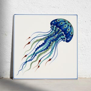 Könnte beinhalten: Eine quadratische Keramikfliese mit einer handgemalten Quallenillustration. Die Qualle hat eine tiefblaue Glocke mit türkisfarbenen und roten Akzenten sowie lange, fließende Tentakel in Blau-, Grün- und Rottönen auf weißem Hintergrund.